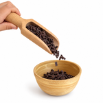 Dark chocolate chips poured by hand from a wooden scoop into a wooden bowl