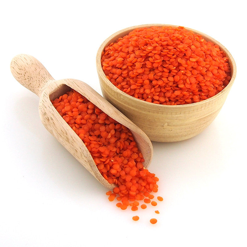 A wooden bowl and scoop filled with red split lentils on a white background.